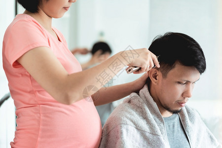 刀具亚洲人国内的年轻孕妇在流行期间在家里的亚洲丈夫用剪刀男人头发亚洲丈夫在家庭理发店隔离式夫妇生活方式时从妻子身上理发图片