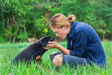 外部狼疮持有年轻的caucasian年轻女狗主人在天然草地上抱着可爱的Rottweiler小狗图片