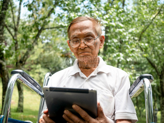 老的坐在轮椅上老人使用数字平板电脑看屏幕阅读电子书在网上与孙子聊天在公园看电影男人退休图片