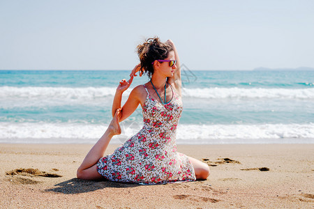 海滨冷静的体式夏天穿着衣服的年轻女子在海边滩上练瑜伽在阳光明媚的白天在海边或图片