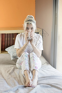 天请享用年轻的金发美女坐在床上喝着一杯咖啡穿睡衣的咖啡在家庭气氛中白种人图片