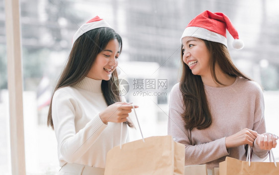 季节女士两名身戴圣塔帽的可爱妇女在圣诞节或新年庆祝活动期间持有纸袋和手晋升图片