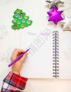 亲爱的圣诞老人信贺卡孩子左手拿着一支笔左撇子在木制背景的白纸上写字新年装饰童梦想的礼物新年概念孩子拿着笔在他的左手一个撇子在木制图片