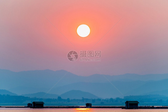 海岸美丽的自然景观橙色太阳在红的天空光下在水湖蓝色山背景在日落时剪影鱼农场笼子村生活方式在Krasiao大坝素攀武里泰国太阳在山图片