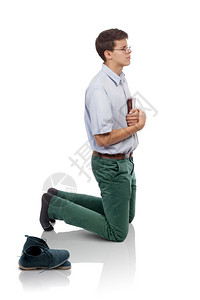 年轻男子谦卑的跪在怀着圣经与一起祈祷的膝盖上一双鞋子放在手后面一