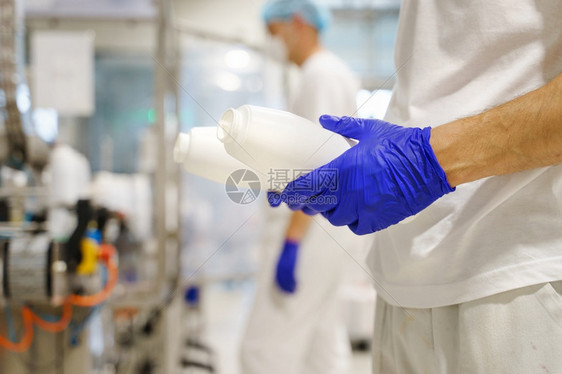 保护的技术工业在厂作时持瓶装容器的不知名天主教男子紧地握住身份不明的人手食品生产蓝橡胶保护手套作为工场所的卫生程序安全概念图片