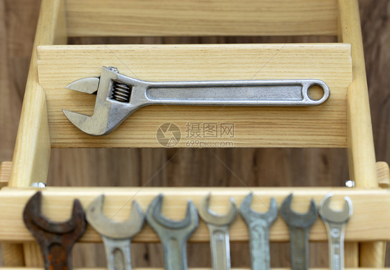 旧的可调整扳手就躺在木制梯子的台阶上其背景是用木制板缝合的旧扳手老建筑工具板条乐器改进图片