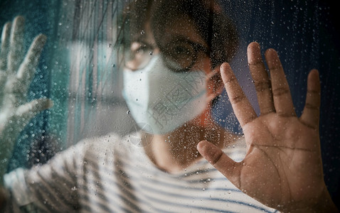 戴着口罩看窗外雨天的男性高清图片