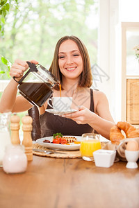 食物积极的笑着caucasian女人在家吃早餐时倒上一顶咖啡帽的照片早晨图片