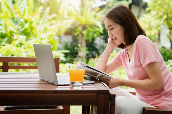 模型喝抓住中年亚洲妇女阅读一本书在家中拿橙汁杯健康保概念和为康而吃东西图片
