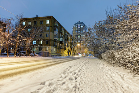 蓝色的户外冬季城市风景街道上一条有雪覆盖的公路市区街道上有住宅建筑和树木在雪中也有树木城市夜间照明是在城市街道上一片蓝色黄昏白雪图片