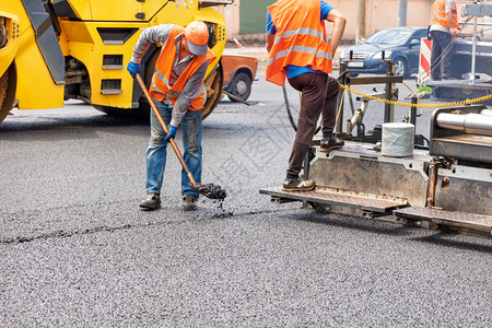 机器建造多层一队道路工人正在沥青摊铺机和压路的帮助下修复一段路在道上铺设一层新的热沥青复制空间一队道路工人正在用业道路机械铺设新图片