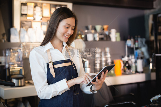 商业女员工接受在线客户的订单在网路用户的批发下亚洲女咖啡师在她的手中微笑着石板女雇员正在接受线上顾客的命令愉快在室内图片