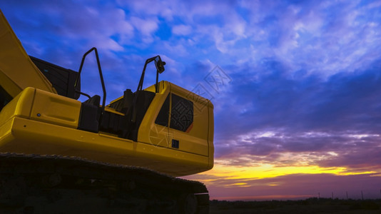 黄昏夏天装载机部分黄色挖土停在建筑工地以低角度和复制空间的彩色双光天空背景对面图片