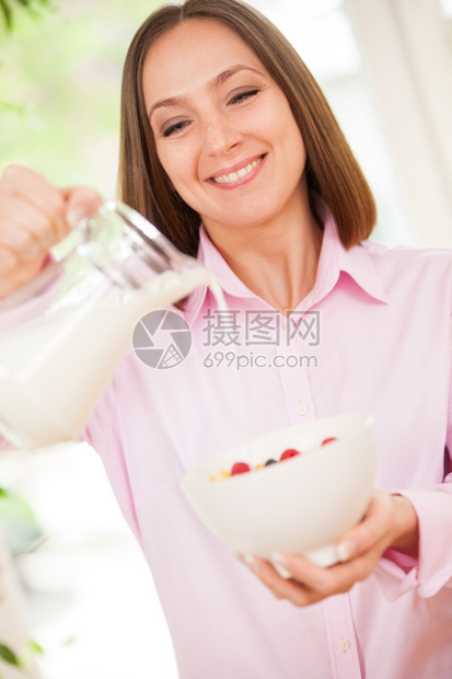 年轻的微笑黑发女人在玉米片中倒牛奶的肖像美食甜图片