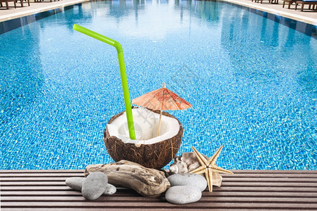 贝壳鸡尾酒加绿色饮用稻草和鸡尾雨伞在游泳池旁边质地果汁图片