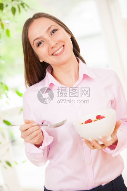 饮食手拿浆果的笑女人着一碗有玉米片的健康谷物图片