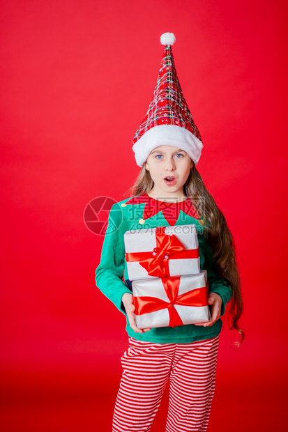 笑游戏传统圣诞快乐迷人的女孩带着礼物穿鲜艳的红色亮背景上的圣诞老人助手精灵服装一个美丽的精灵婴儿肖像复制空间圣诞快乐带着礼物的快图片