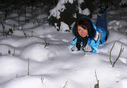 一个穿着温暖的蓝色冬季夹克快乐年轻白人女子躺在雪堆里微笑着女孩脸上的快乐情绪冬夜快乐的年轻白人女子躺在雪堆里女孩脸上的快乐情绪说图片