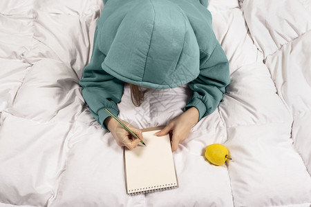 连帽衫一个女孩在现代舒适的家床上笔记本写成的顶端视图创意概念Banner复制空间观在现代舒适的家床上用笔记本写成的女孩上顶端视图图片