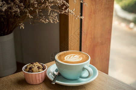一种棕色的烘烤咖啡馆店早餐在商业工作概念期间在咖啡馆的店里吃早餐在商业工作构想中与茶杯的拿铁热咖啡和艺术牛奶泡沫加拿铁粉杯以及木图片