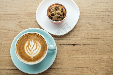木制的甜点咖啡馆店的早餐在商业工作概念期间在咖啡馆的店里吃早餐在商业工作构想中与茶杯的拿铁热咖啡和艺术牛奶泡沫加拿铁粉杯以及木桌图片