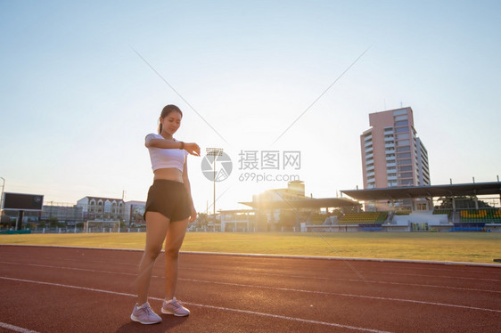 运动的美丽年轻亚裔妇女正在观看体育手表或智能在体育场赛道上慢跑健康生活方式和运动概念图片