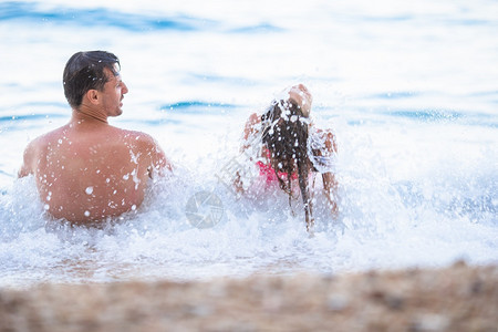 年幼父亲和他的小女儿在海浪中玩得开心暑假家庭节日父亲和女儿享受海滩度假喜悦微笑晴天图片