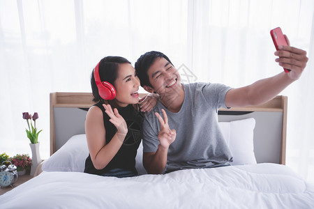浪漫爱亚洲情侣躺在家里玩手机和自拍的床上躺在游戏手机上图片