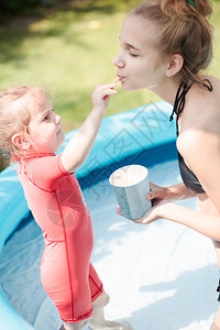 快乐的开支朋友们年幼少女和她妹在游泳池里玩夏日享受吃冰淇淋的暑假时间图片