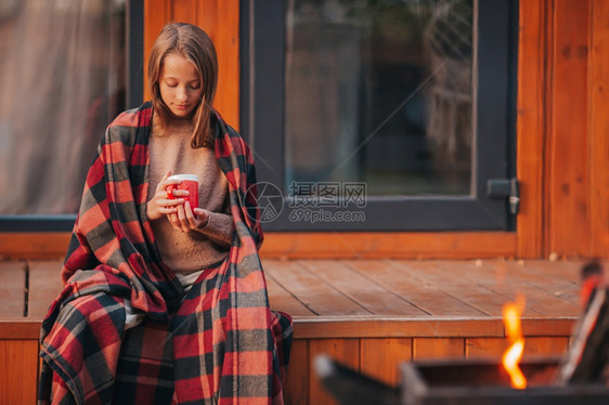 愉快在秋天温暖的日子里穿着毯裹毛的美丽女孩喝着热饮的漂亮女孩秋天在阳台上享受着秋天热的放松图片