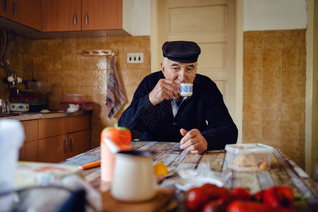 人们身着黑色毛衣和帽子在家中单坐的桌子边喝咖啡或茶的一杯高级男子曾祖父老的养金领取者图片