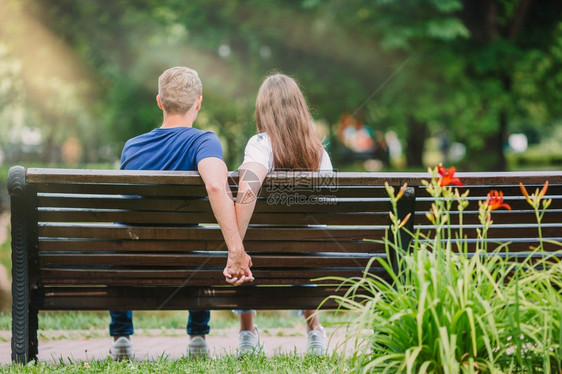 微笑淑女坐在公园长椅上的年轻漂亮一对夫妇手牵在公园长凳上放松的年轻家庭英俊图片