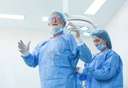 面具助手外科医生帮在院手术前穿着制服的高级医生女援助在医院做手术前帮助妇女图片