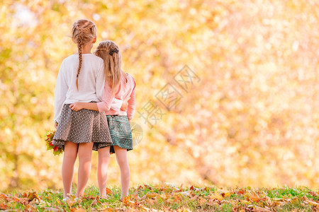 在秋天温暖的阳光明媚日子里户外可爱的小姑娘们温暖的秋天父母树叶灰色的图片