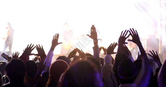 流行音乐会群众在节日观看后举手向明亮的舞台灯升起发光的受欢迎图片
