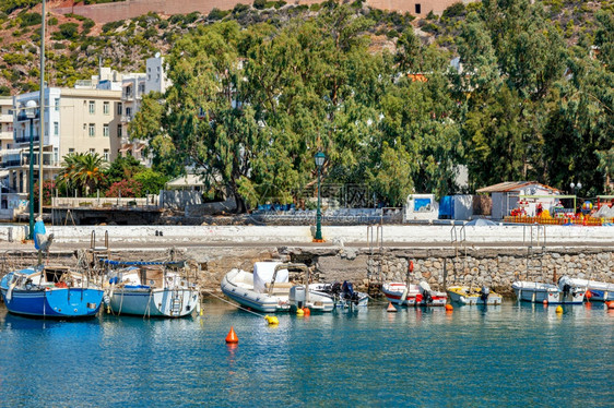 希腊语夏天旧渔船摩托艇停泊在爱奥尼亚海湾码头背景是城市公园的棕榈树林和希腊Loutraki的山坡和小船停泊在爱奥尼亚海清澈的水中图片