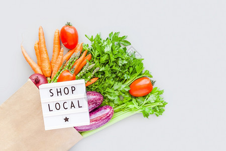 新鲜的在生态手工艺纸购物袋中的新鲜有机蔬菜中在灯箱平板上装有文本的当地商店LocalShopFlooronlightboxfla图片