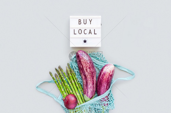 绿色棉花网状购物袋中的新鲜有机蔬菜与文本BuyLocal在灯箱平铺上买本地公司在灰色背景的复制空间中以顶视图显示可持续生活方式零图片