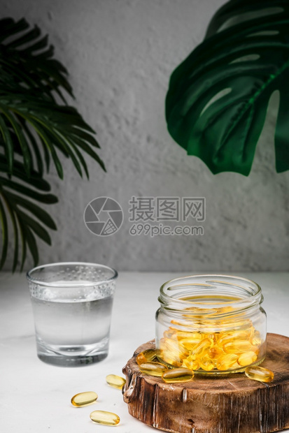 在木架上的玻璃罐旁边一杯水中用蛋白3和维他命D胶囊贴上鱼油保健概念是FishOilSoftgels营养的治疗喝图片