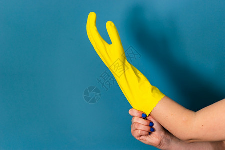 近距离紧贴着不明的caucasian女孩的手她们要求调整持有保护黄色橡皮手套以便白天对蓝墙背景进行清洁或消毒冠状病在室内人类图片