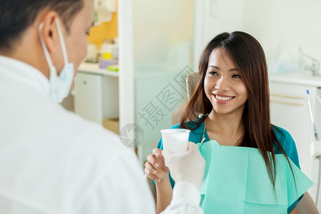 药物笑着的亚洲女人正在从牙医那里取水杯程序一种图片