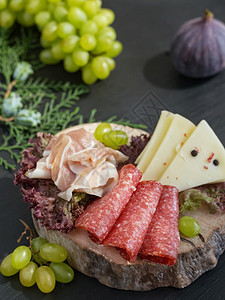 切片的腊肠培根奶酪切片放在木制板上一块沙拉纸的黑石岩本底葡萄和无花果红色的三明治木制图片