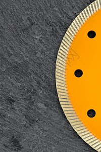 蛮横的工具结石钻切割车轮的一部分其中含有切碎石块和花岗岩的薄切片深灰色花岗岩背景上的黄色圆圈复制空间垂直图像黑色灰花岗岩背景上的图片
