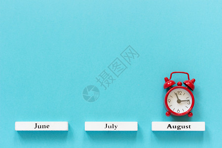 木制的喜庆典木制日历夏季月份和8在蓝色背景上的红闹钟概念八月时间图片