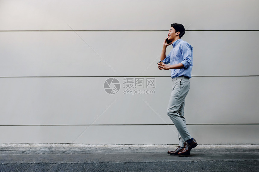 工作满的办公室在城市建设中走现代人侧面观全长的城墙生活方式之旅时使用移动电话进行临时穿戴的快乐青年商人图片