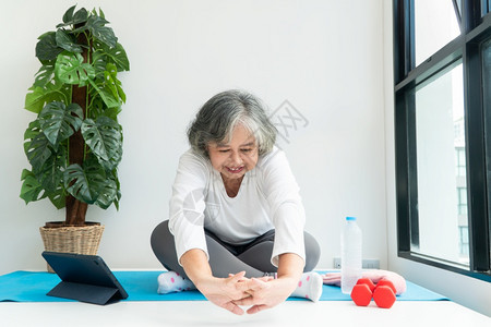 上笔记本电脑在线课程的亚洲老年妇女在家中起居室练习时观看膝上型计算机在线课程网上锻炼培训概念平衡班康复图片