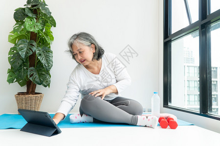 女重量上笔记本电脑在线课程的亚洲老年妇女在家中起居室练习时观看膝上型计算机在线课程网上锻炼培训概念体操图片