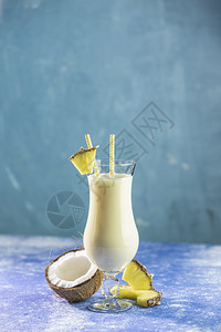 可乐达果汁以蓝混凝土背景配上一片菠萝装饰的冰冻PinaColada加勒比传统鸡尾酒杯奶昔图片