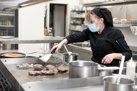 工人戴防护面罩的女厨师在餐厅或酒店的厨房准备食物冠状预防概念高质量照片戴防护面罩的女厨师在餐厅或酒店的厨房准备食物冠状预防概念服图片